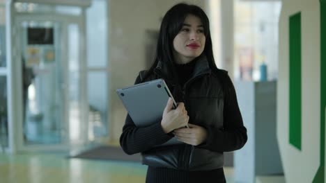 professional female manager in a black formal outfit, walking through the office, interacting with colleagues, holding documents and a laptop, showcasing leadership and professionalism