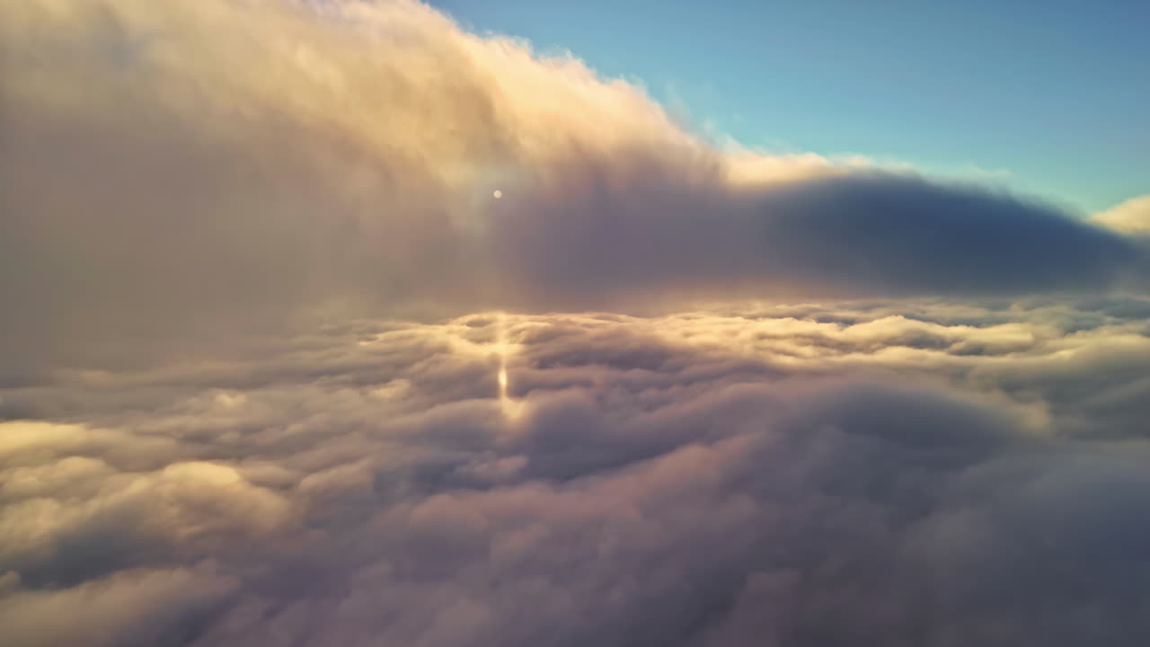 Drone moves forward and gently descends through warm golden clouds, revealing a calm illuminated cloud layer glowing under the soft sunlight