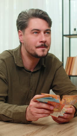 middleaged man counts cash smiling showing big financial success euro bills wealth at table desk