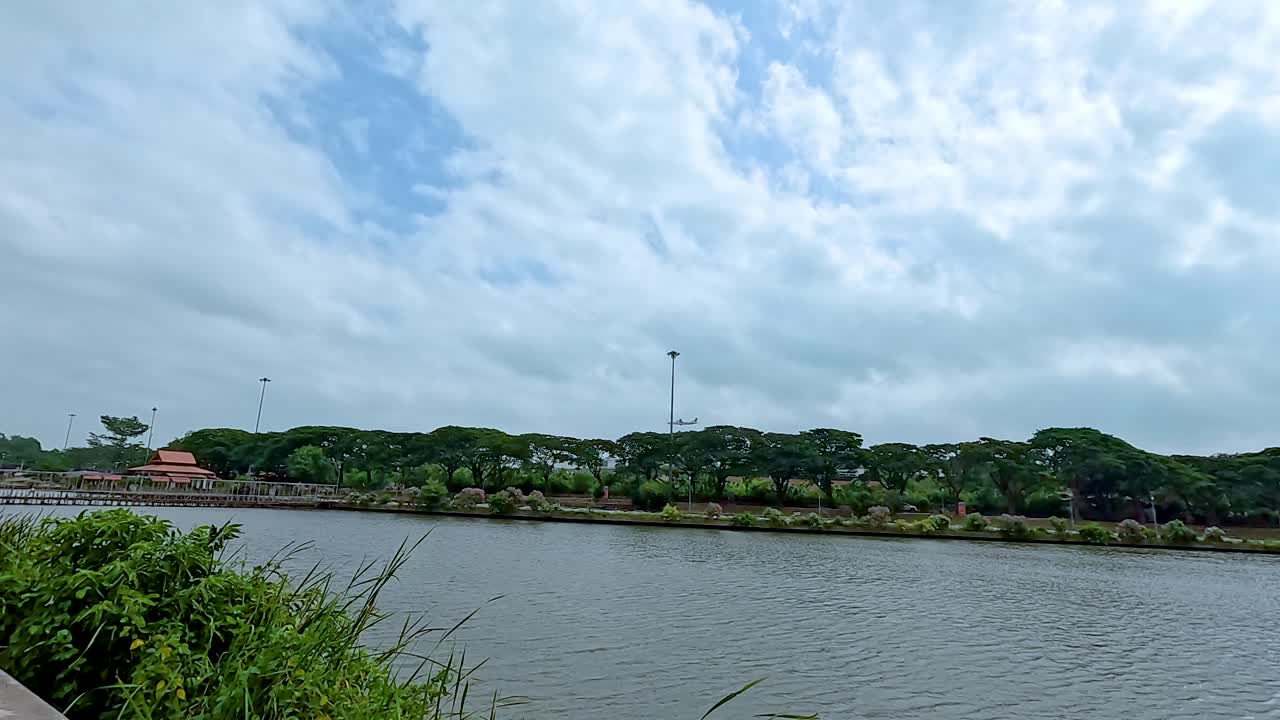 A tranquil riverside path in Koh Samui with lush greenery and a calm river under a partly cloudy sky