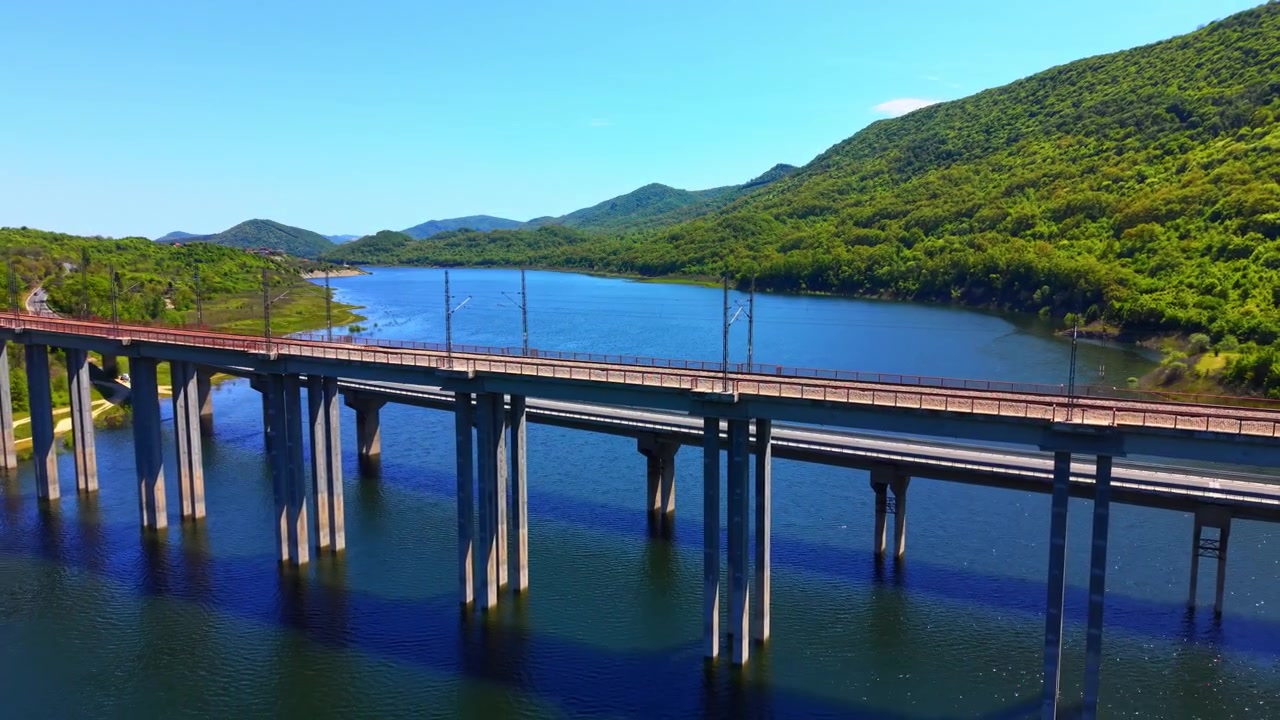 貯水池にかかる鉄道橋。青い水面と丘陵地帯の上にコンクリートの支柱で支えられた電化された線路の高所からの眺め。