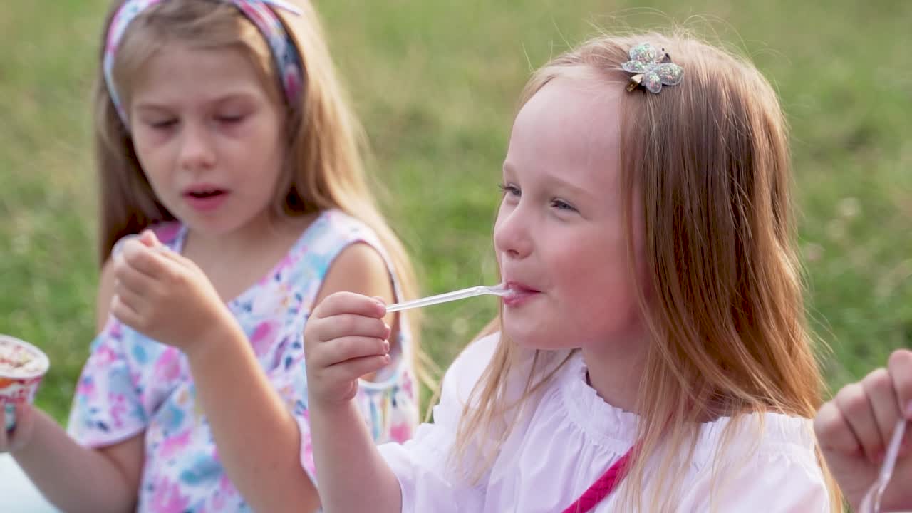 Amiche felici mangiano il gelato con un cucchiaio sedute sull'erba verde. Primo piano al rallentatore