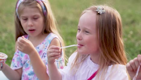 happy girls girlfriends eat ice cream with a spoon sitting on the green grass. slow motion close-up