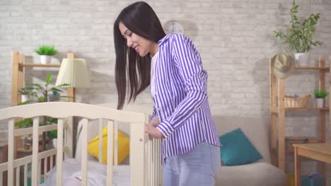 portrait of a positive young asian mom next to a baby cot in the living room