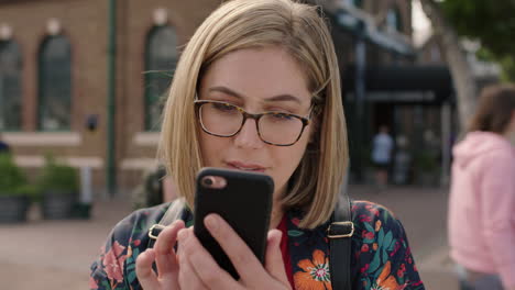 portrait of young blonde woman texting browsing using smartphone social media app wearing glasses in urban background