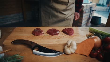 juicy steak pieces with spices on a wooden board, knife, fresh veggies, rustic mood