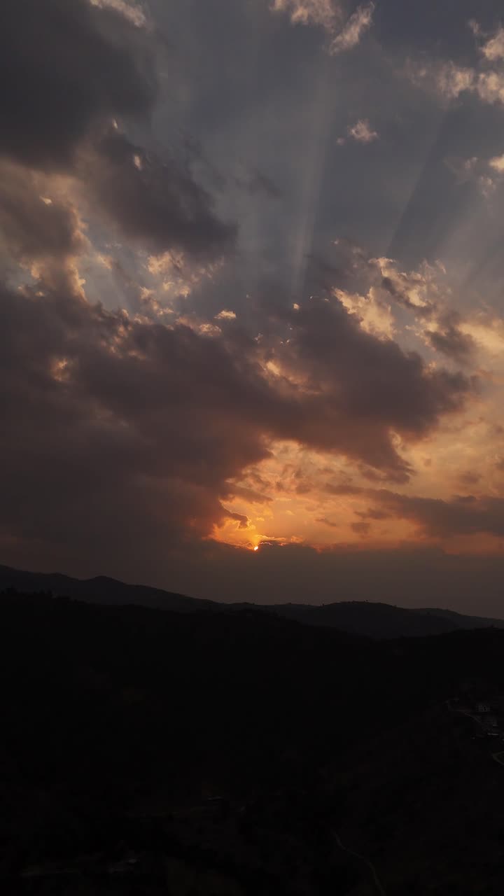 A vertical view of the sunset behind clouds, with single rays of sunshine breaking through.
