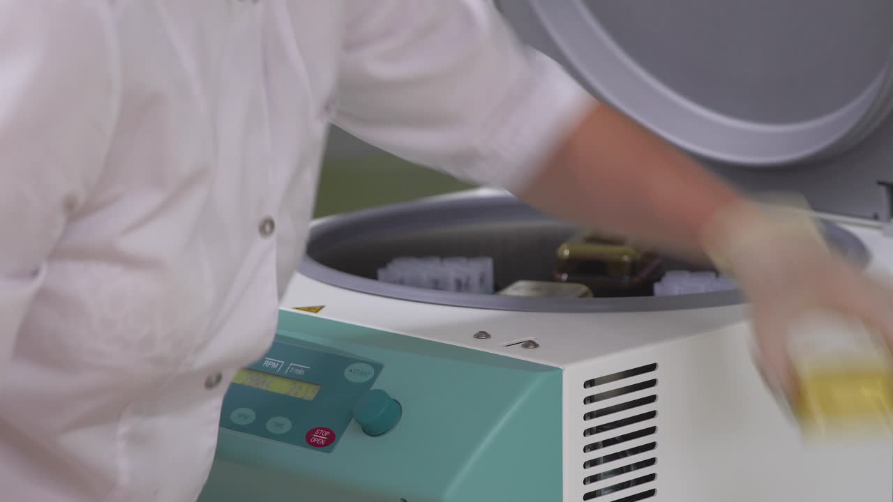 In the laboratory, a woman in a Bathrobe and gloves sets human cell samples in test tubes in a centrifuge to untwist and separate the extra layers of cells. Opens the lid and pulls out the test tubes