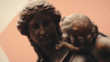 close up of an ancient antique female statue holding a small child in a museum with moody warm lights