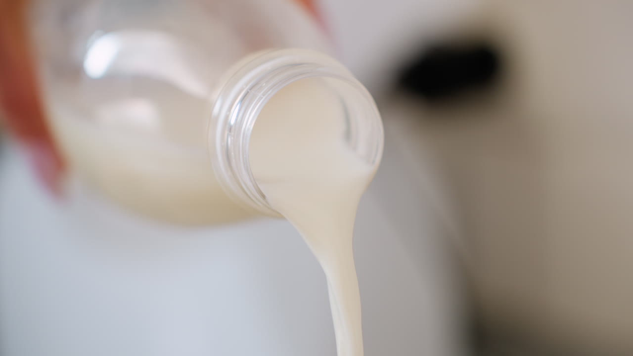 Close up of fresh yoghurt being poured from bottle with blurred background, creamy liquid texture highlighted in focus, concept of healthy dairy nutrition, breakfast preparation