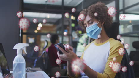 animación de células de covid-19 sobre una mujer limpiando un teléfono inteligente en la oficina con una máscara facial