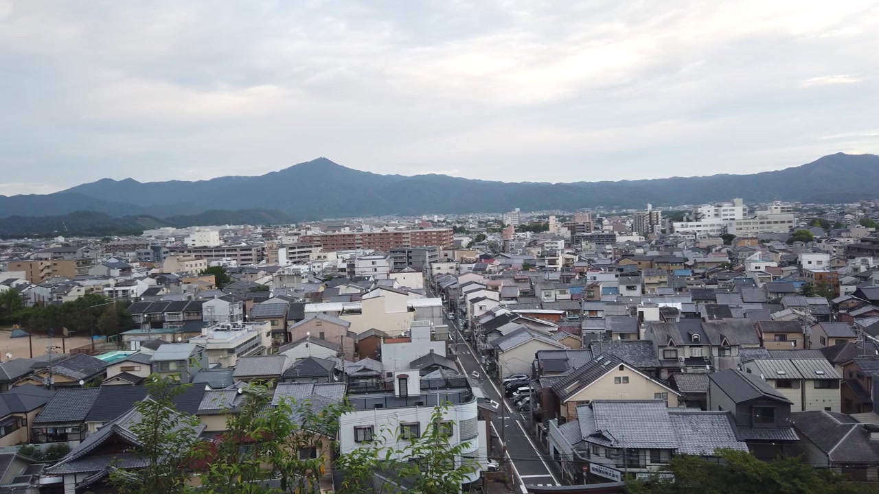 Panoramica aerea del paesaggio urbano di Kyoto, Giappone, con una strada asfaltata e tranquilla con vegetazione, un quartiere residenziale e uno sfondo montuoso, ampio orizzonte.