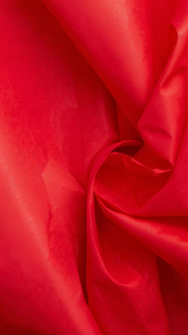 Vertical video: Showing red fabric spiral tightening from tiny shift in tight closeup, satin sheen
