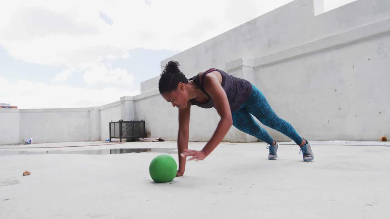 mujer afroamericana haciendo ejercicios de flexión en una pelota de medicina en un edificio urbano vacío