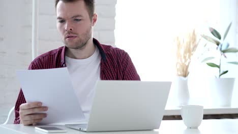 young man reading documents and working on laptop