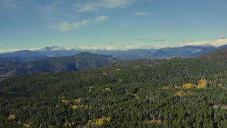 Aerial-looking-out-over-fall-forest-with-changing-yellow-aspens-to-mountains,-4K