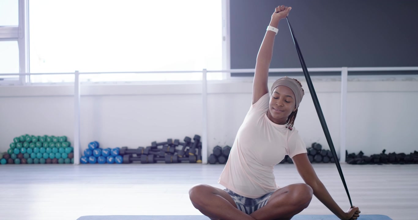 African American adult woman anchoring strap left hand pulling stretching for mobility on blue mat