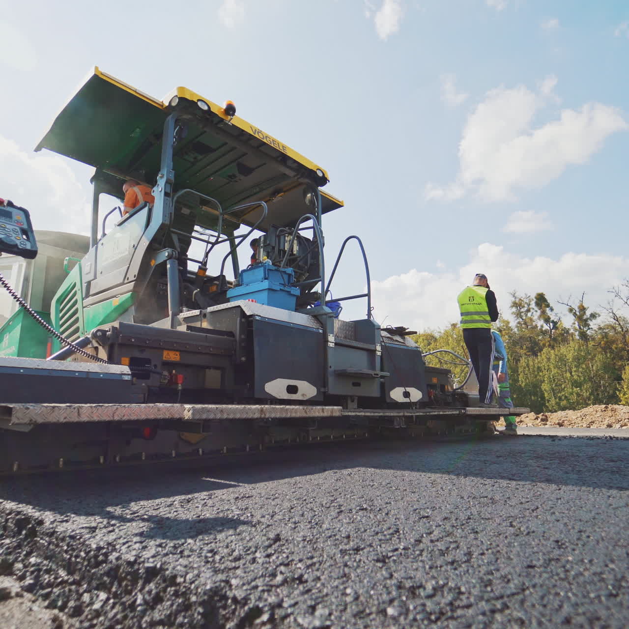 Asphalt paver machine and workers during the road construction. Heavy machine for paving applying fresh asphalt. Man worker on the paver machine with special equipment.