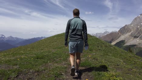 Hiker-walking-on-top-of-mountain-plane-revealing-peak,-Rockies,-Kananaskis,-Alberta-Canada