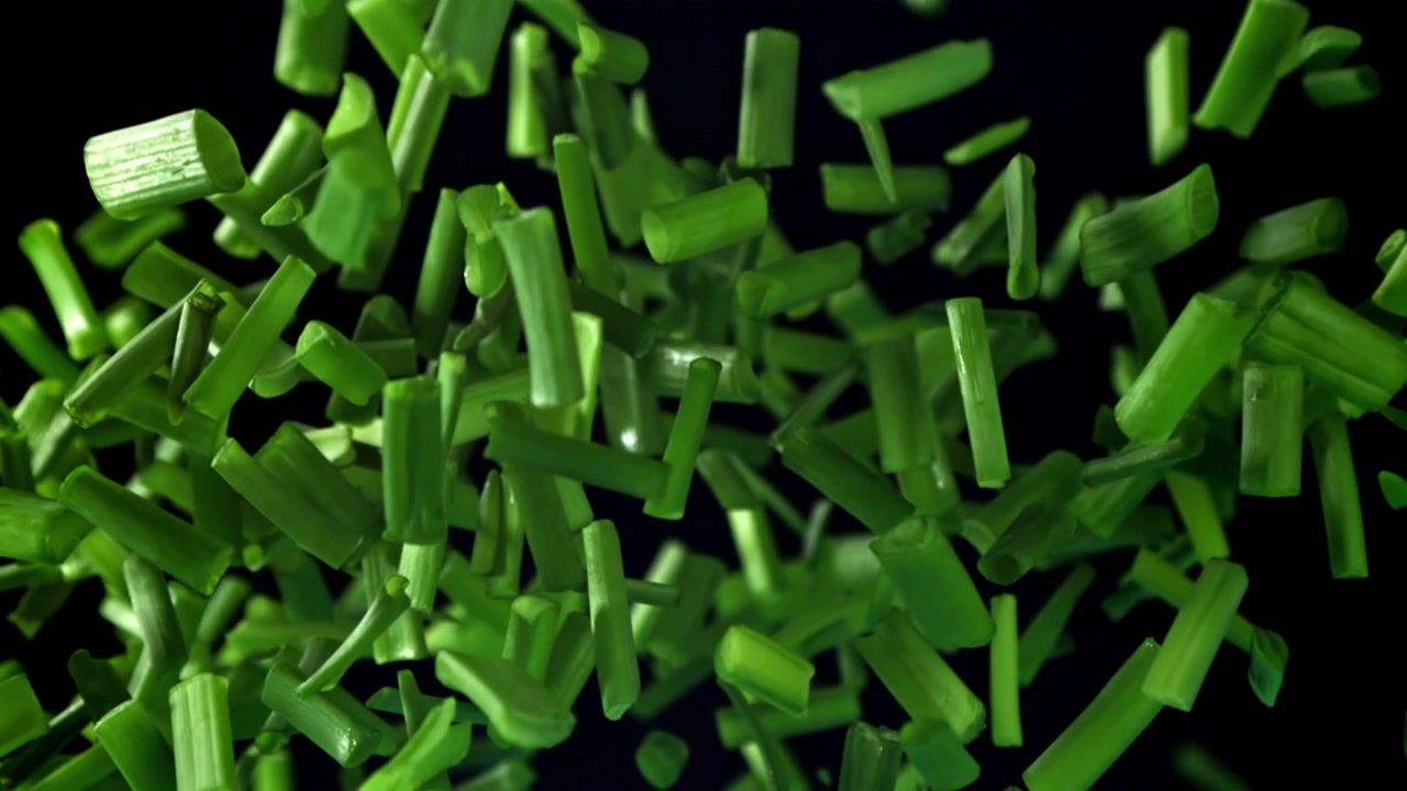 Hakkede forårsløg falder i slowmotion på sort baggrund.