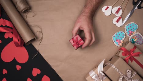 one male hand rotates a small red box on the table. hearts and wrapping paper. valentine's day gifts concept