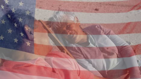 Animation-of-flag-of-united-states-of-america-over-senior-biracial-couple-in-deckchairs-on-beach