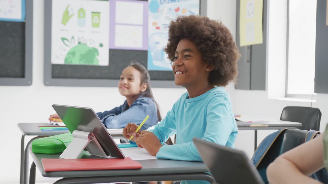 Video di scolari felici di diverse etnie seduti ai banchi con i tablet, che ascoltano in classe, con spazio copia.