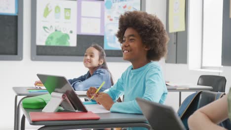 Video-of-happy-diverse-schoolchildren-sitting-at-desks-with-tablets,-listening-in-class,-copy-space