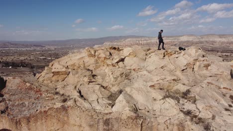 aventura de capadocia: excursionista turístico en solitario se sienta en la cima de la vivienda de la cueva de la montaña disfrutando de la vista hacia göreme y el castillo de uchisar en el horizonte