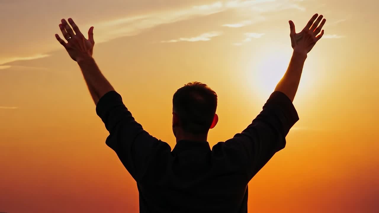 Businessman stands with arms raised at sunset, embodying a moment of celebration and victory. The silhouette against the vibrant sky symbolizes hope and new beginnings