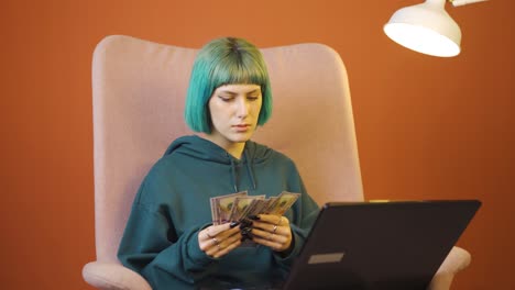 Young-woman-looking-at-laptop-counting-money.