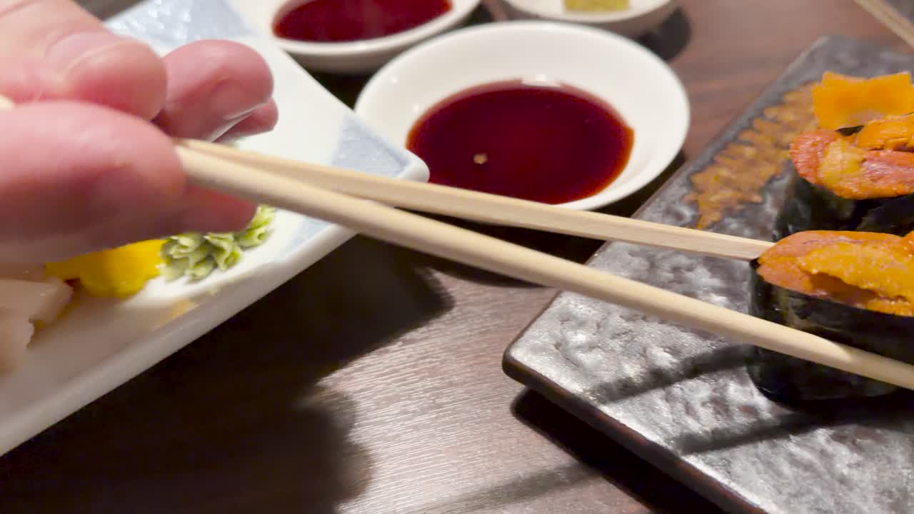 Close-up of assorted sashimi and uni sushi, hand with chopsticks, warm restaurant lighting, steady camera