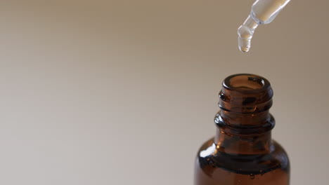 Video-of-make-up-bottle-and-pipette-with-clear-drops-and-copy-space-on-brown-background