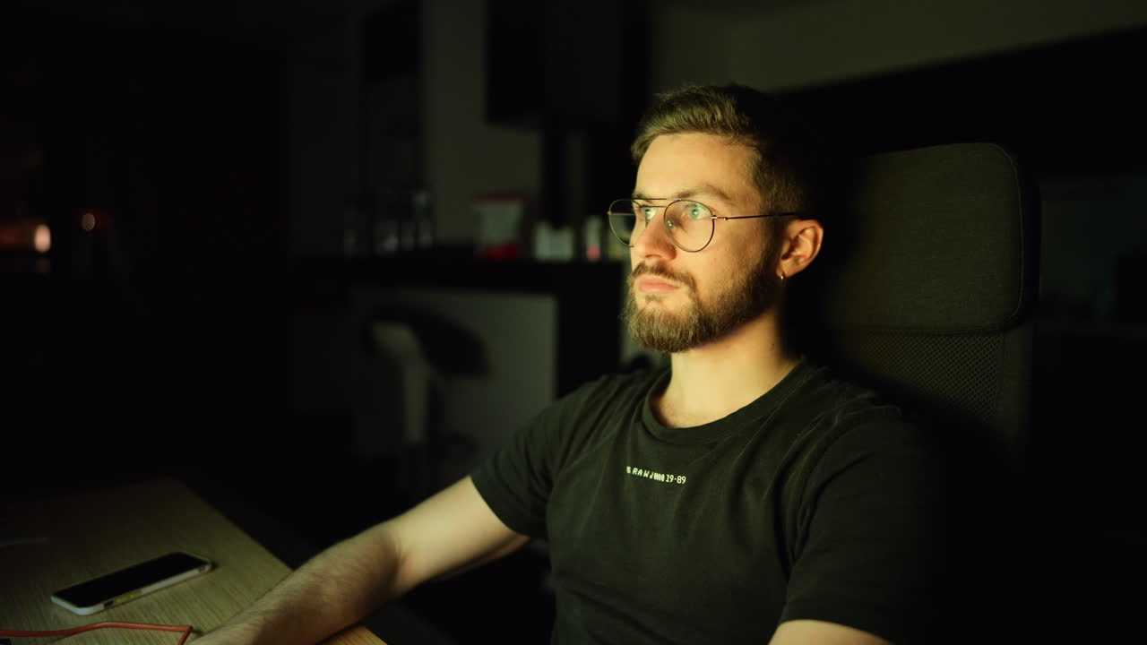 A young man focused at his desk late at night, illuminated by the glow of his screen. A cinematic scene capturing dedication, solitude, and late-night productivity in a modern home office