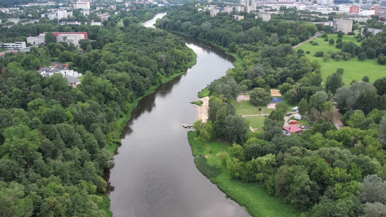 Vista aerea del fiume Neris che serpeggia accanto a una piccola spiaggia sabbiosa, sponde boschive e spazi verdi aperti a Vilnius in una tranquilla giornata estiva