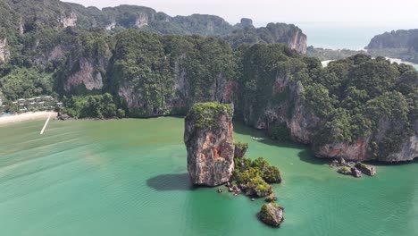 amazing aerial over tall rock reveal small resort on remote beach in krabi, thailand.
