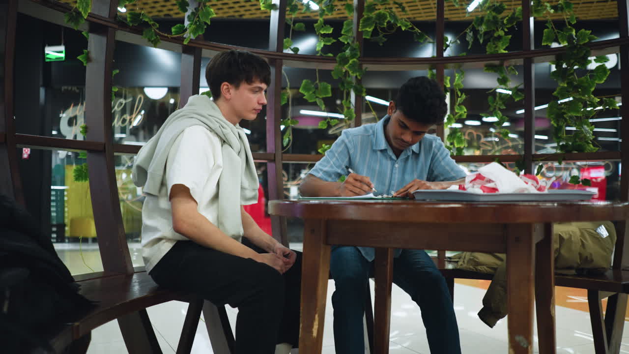 Full view of two teenagers sitting on wooden chairs at vintage desk writing notes,over paper with pens under warm ambient light capturing focused study session and creative collaboration mood joy