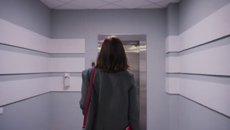 businesswoman walking down modern office hallway toward elevator with briefcase, wearing formal attire in professional setting. corporate environment, career, business concepts