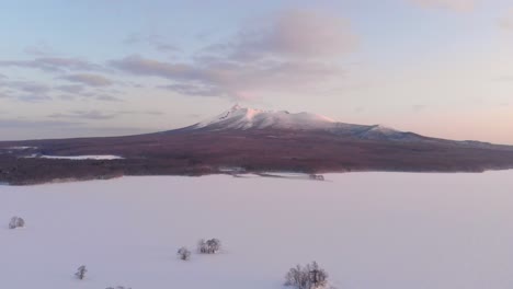 slow aerial pull back over beautiful snow capped mountain and snowy landscape at sunrise