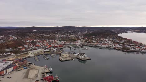 beautiful grimstad city and coastal marina during early morning with reflections in sea - high altitude aerial overview descending and approaching idyllic marina bay close to sea surface - norway