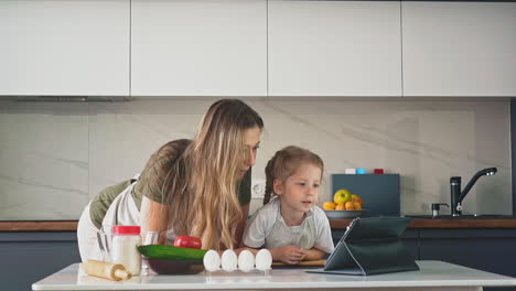 Niña-Y-Madre-Ven-Un-Video-Blog-De-Comida-En-La-Mesa-De-La-Cocina.