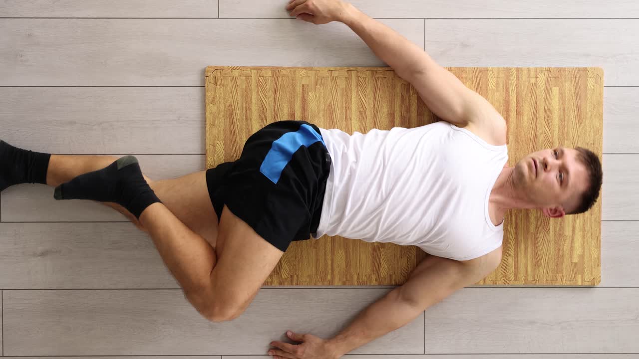 Man does relaxing exercise lying on wooden panel on floor