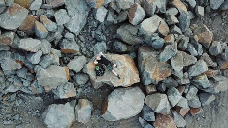 bald man lays on a large stone. tourist with a backpack in shorts and t-shirt is resting. aerial view
