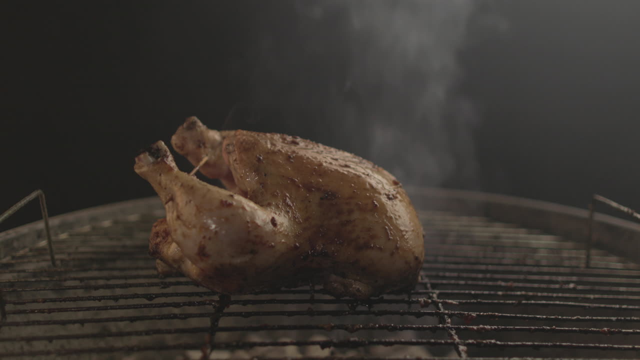 Poulet grillé sur des braises et du feu, avec de la fumée s'élevant, sur fond noir, filmé en RAW et 4K à hauteur des yeux