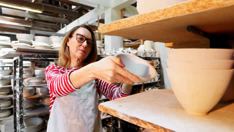 Female-potter-arranging-bowl-in-shelf-4k