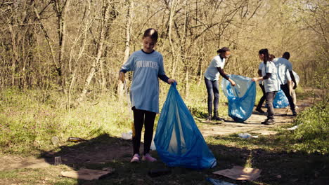 Una-Niña-Pequeña-Recogiendo-Basura-Alrededor-De-Un-Bosque-Con-Una-Herramienta-De-Garra-Y-Bolsas-De-Basura