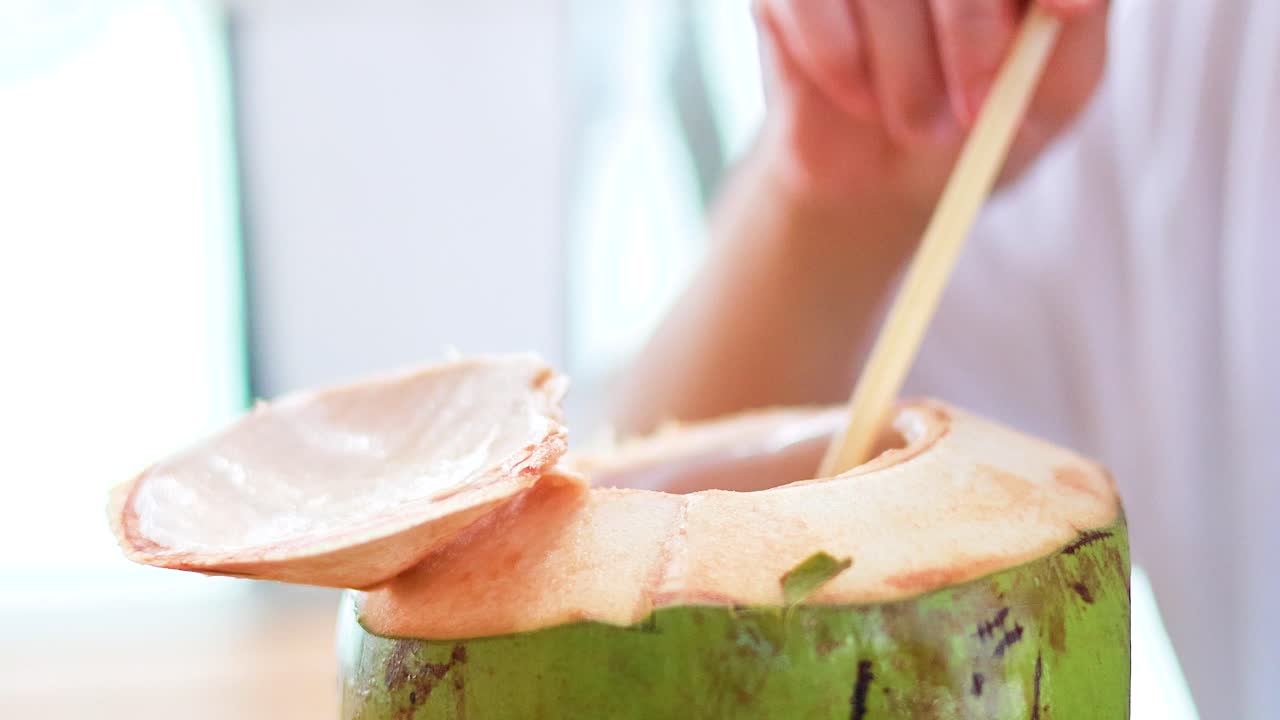 A hand inserts a straw into a fresh coconut under bright, natural lighting in Phuket, Thailand