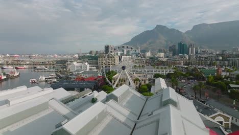 Fly-over-Victoria-Wharf-Shopping-Centre-on-waterfront.-Revealing-The-Cape-Wheel-attraction.-Giant-observation-wheel-in-Victoria-and-Alfred-Waterfront.-Cape-Town,-South-Africa