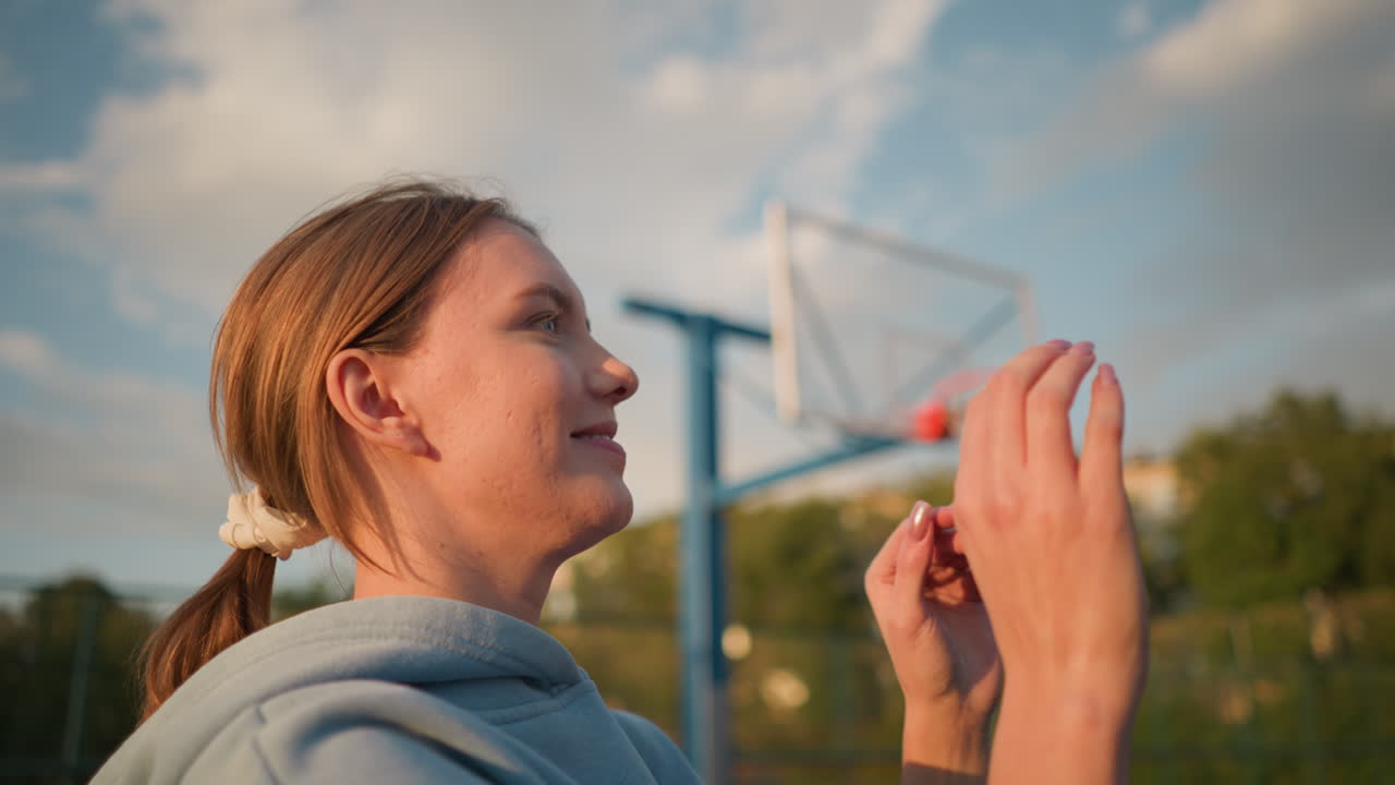primer plano de una mujer sonriente con suéter azul disfrutando de un juego de voleibol al aire libre, brazos levantados en movimiento con vegetación y edificios en el fondo, bajo la luz del sol brillante