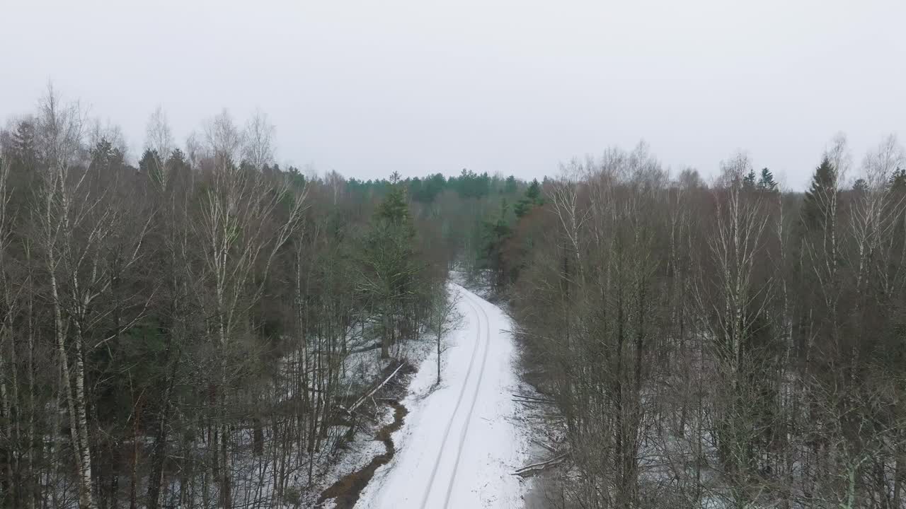 Aerial establishing view of Nordic woodland forest covered with light snow and a dark river , rural road, overcast winter day, low clouds, wide drone shot moving forward